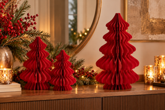 Tre Decori Pino Origami New Rosso EDG Enzo De Gasperi H 20, 30 e 40 cm in carta pieghettata tridimensionale, ambientati su una madia elegante con rami di abete, bacche rosse e candele dorate per una raffinata composizione natalizia.
